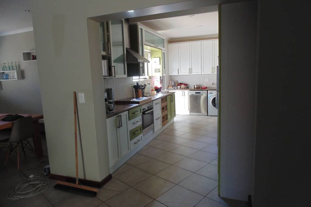 A functional kitchen featuring built-in cabinetry, integrated oven, extractor fan, and tiled flooring, viewed from an adjacent living area.