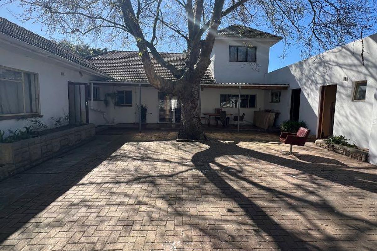 Spacious rear courtyard featuring paved flooring, a large mature tree, and covered patio areas connecting to the main house structure.