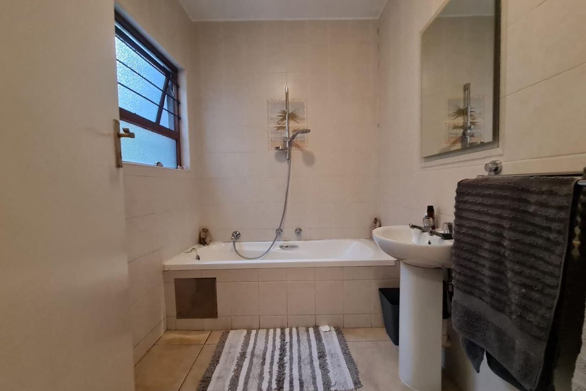 A functional bathroom featuring a built-in bathtub with shower attachment, pedestal basin, and wall-mounted mirror, finished with neutral wall and floor tiles.