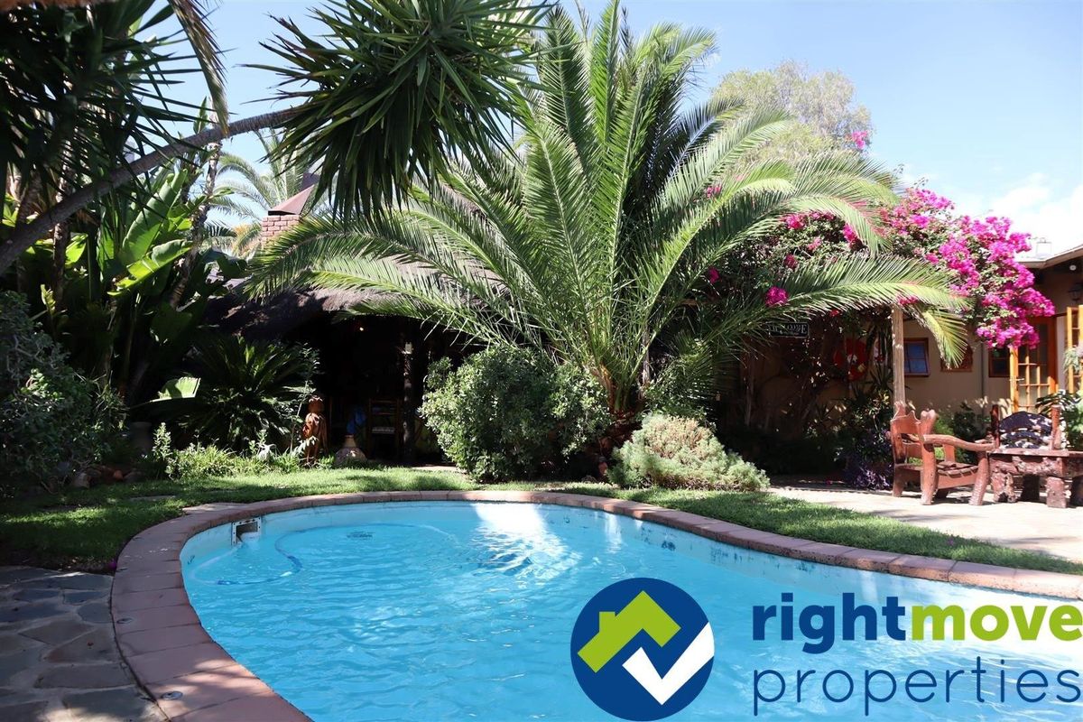 A well-maintained outdoor pool area featuring a swimming pool with brick coping, surrounded by lush garden landscaping and a covered patio space.