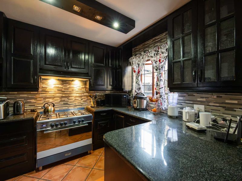A well-appointed kitchen featuring dark cabinetry, granite countertops, a gas stove with extractor fan, and a decorative tiled backsplash.
