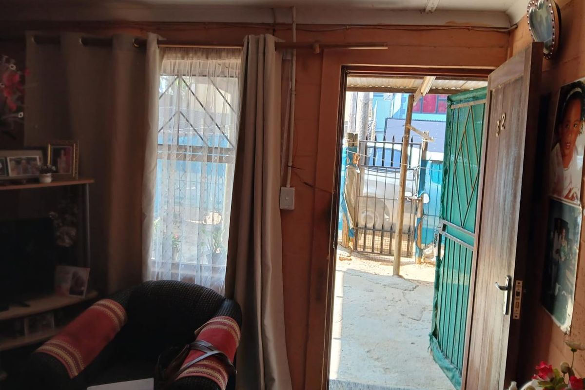A living room area featuring a timber entrance door with a security gate and a window with burglar bars, showing signs of wear.