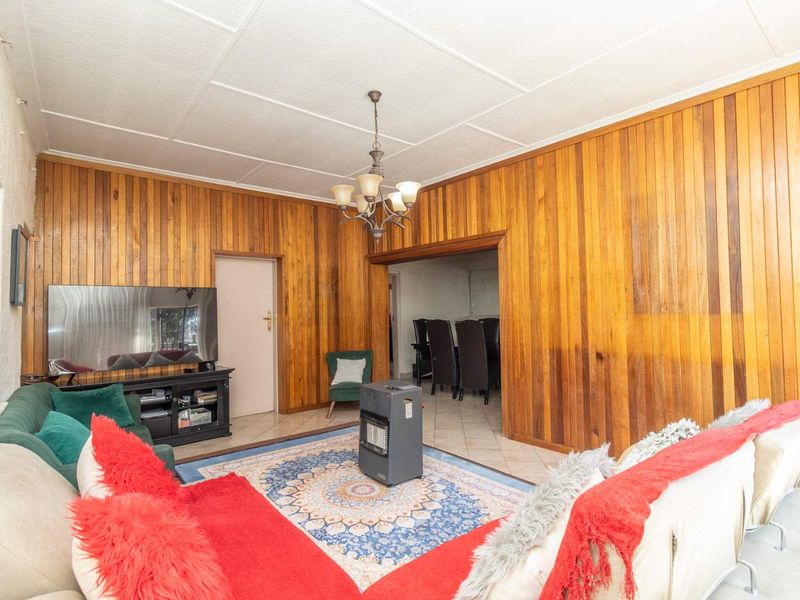 A living room featuring timber wall paneling, tiled flooring, and a central chandelier, providing a traditional aesthetic with potential for modernization.