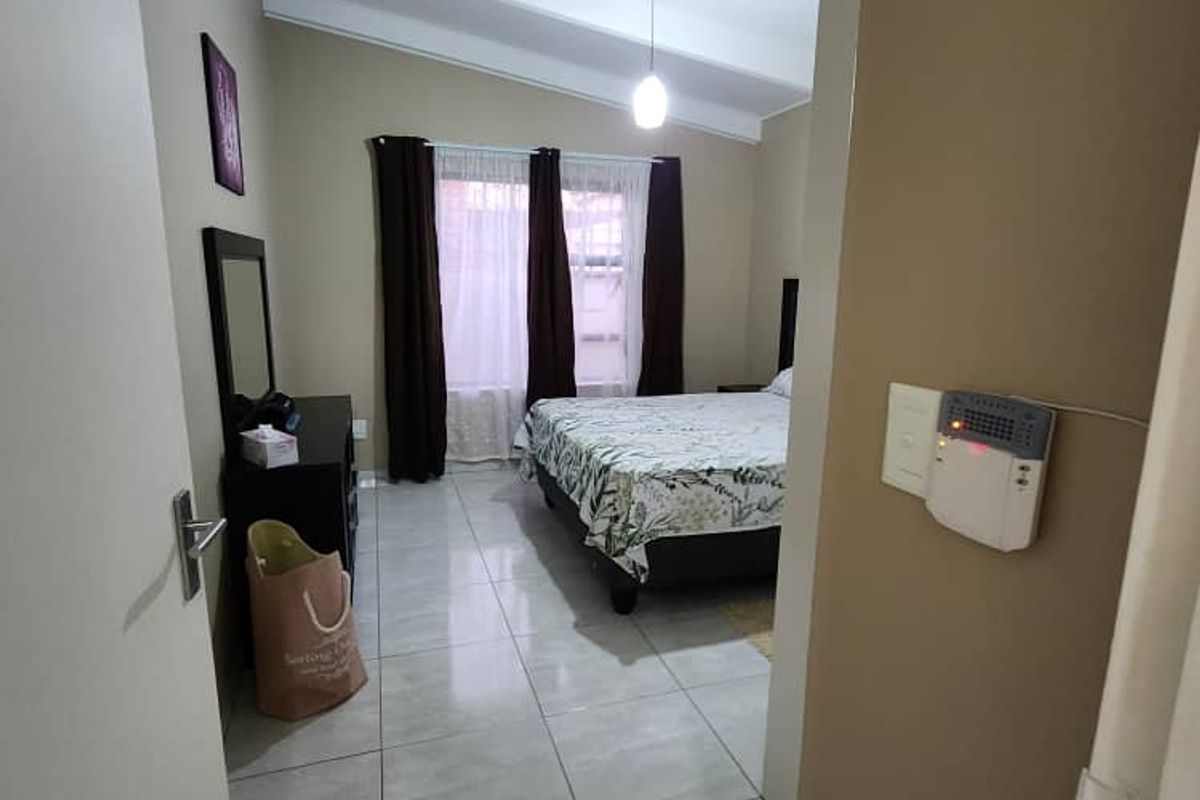 A bedroom featuring tiled flooring, a vaulted ceiling with exposed beams, and a wall-mounted security alarm panel near the entrance.