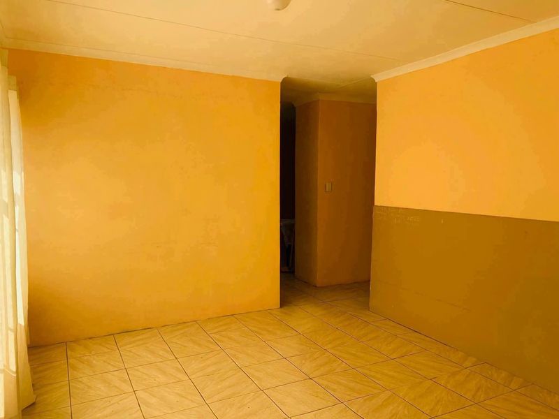 An empty living area featuring tiled flooring and coved ceilings, requiring cosmetic updates to the wall finishes.