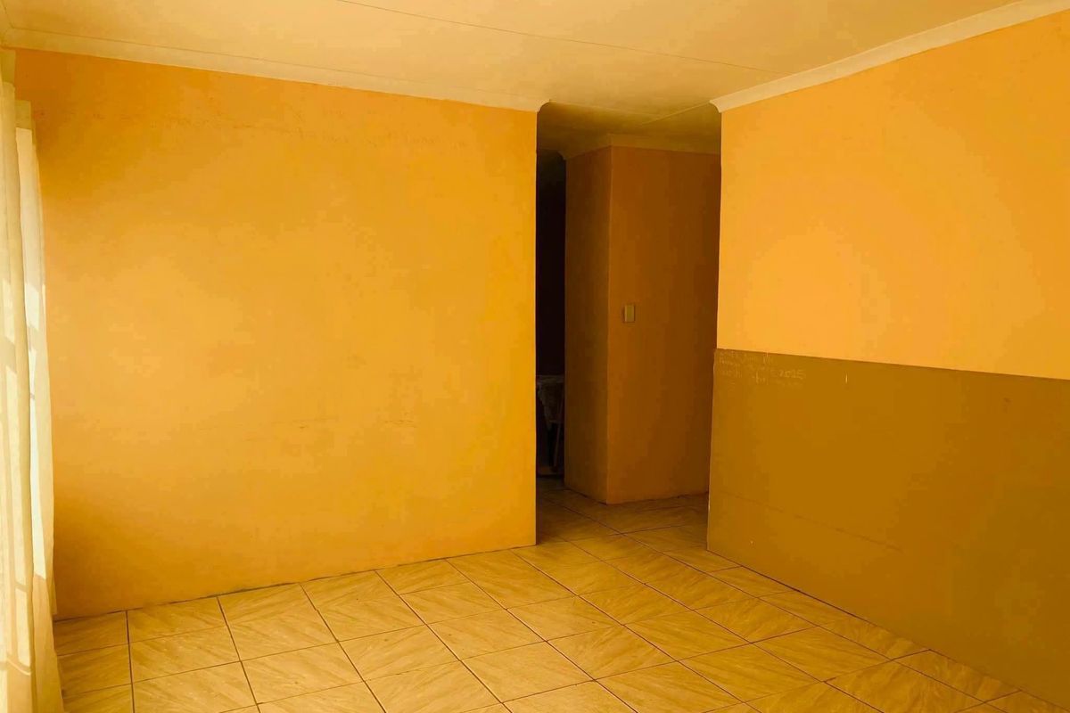 An empty living area featuring tiled flooring and coved ceilings, requiring cosmetic updates to the wall finishes.