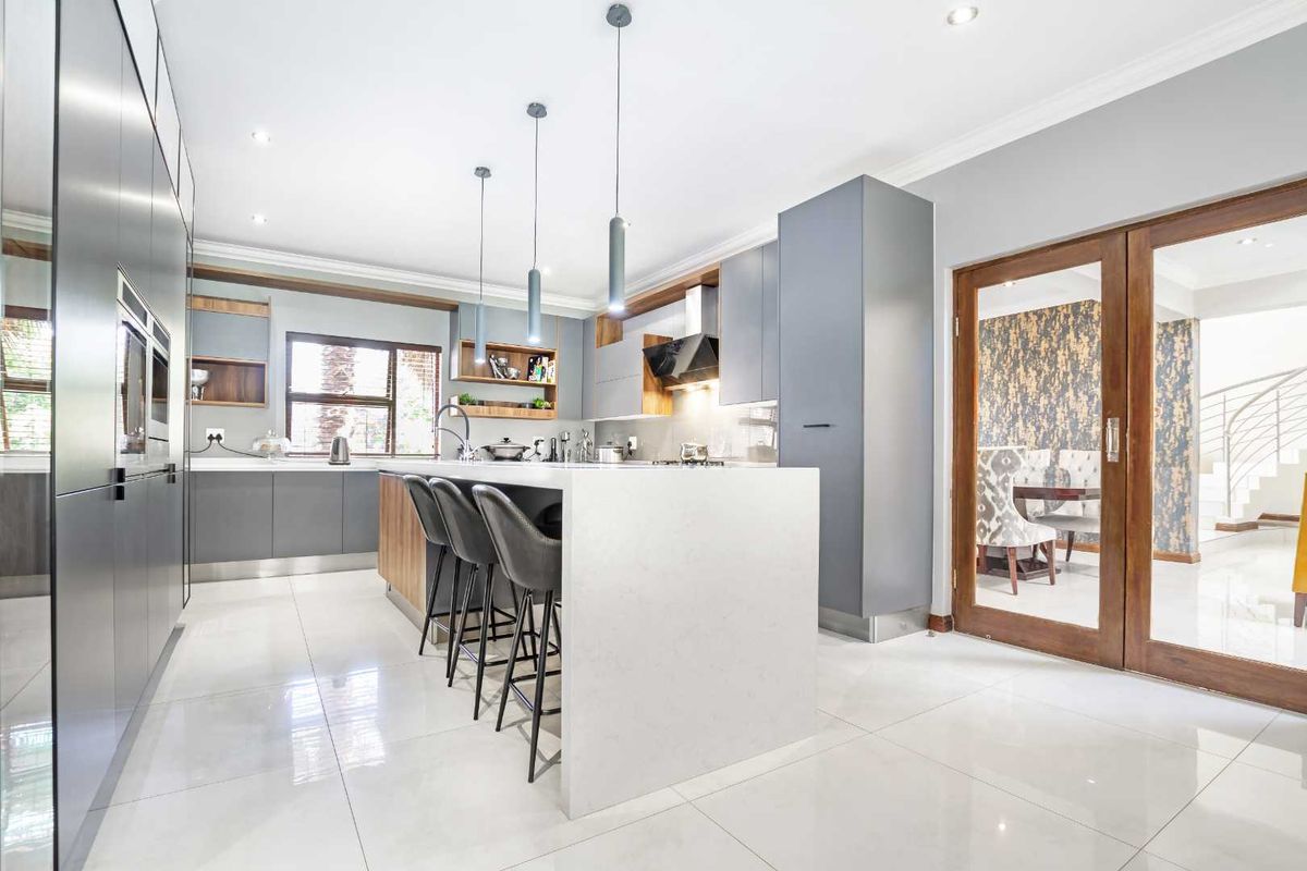 Modern kitchen featuring sleek grey cabinetry, a large central island with stone countertop, integrated appliances, and polished tile flooring.