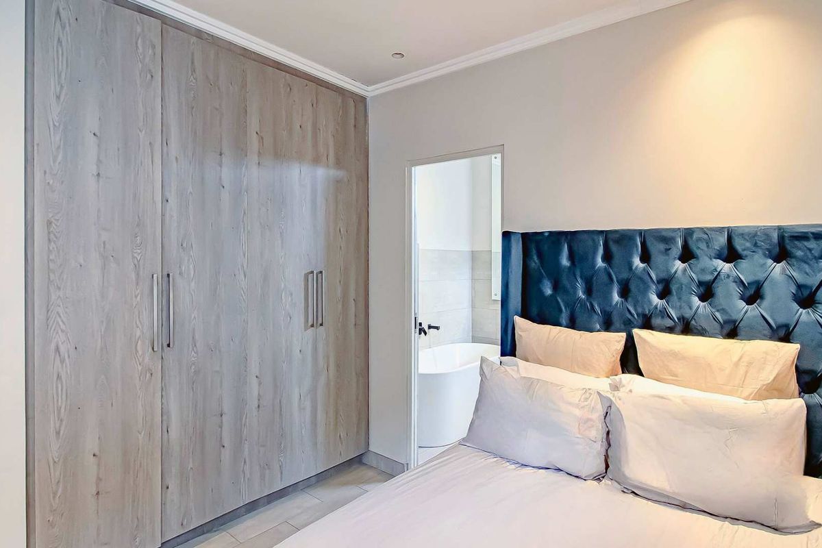 A well-maintained bedroom featuring built-in wood-grain cupboards and direct access to an en-suite bathroom with a freestanding bathtub.