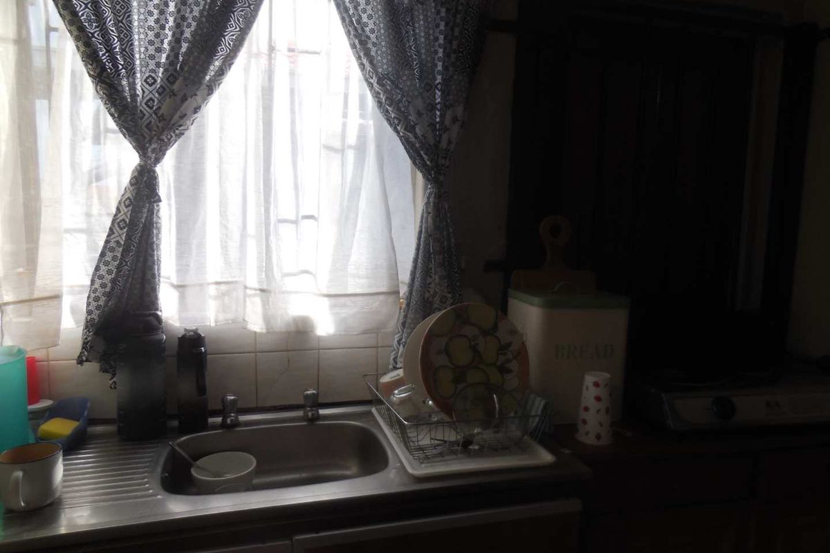 A functional kitchen area featuring a stainless steel sink, tiled splashback, and built-in cabinetry, requiring modernization to improve aesthetic appeal and utility.