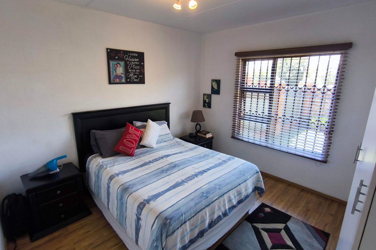 A well-lit bedroom featuring wood-look laminate flooring, a window with fitted blinds, and built-in wardrobe storage.