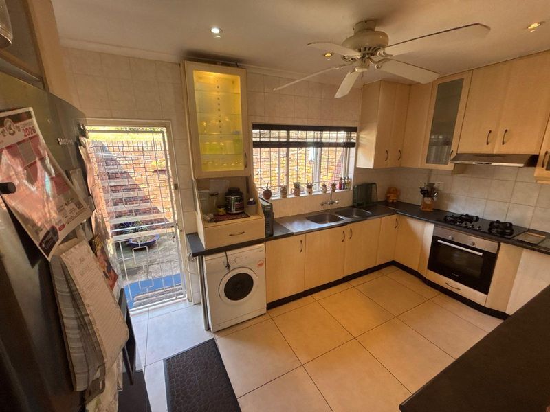 Functional kitchen featuring light wood cabinetry, built-in oven and hob, double sink, and direct access to the exterior via a security gate.