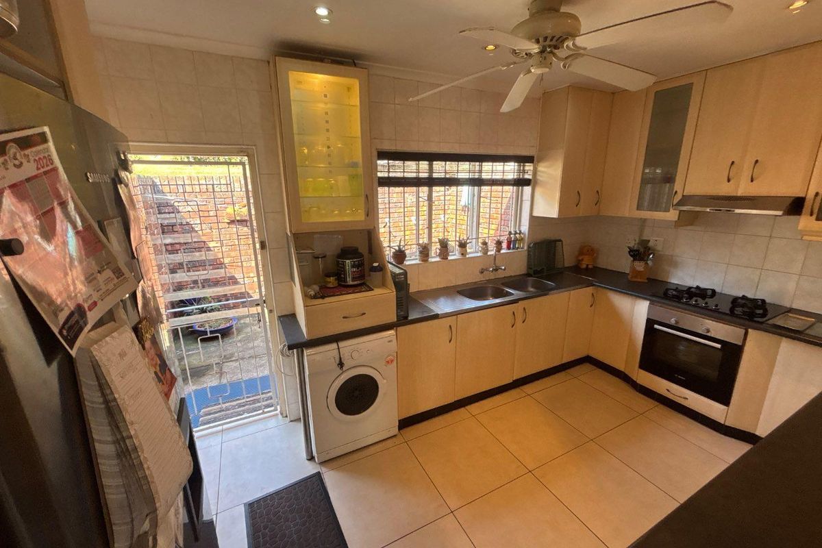 Functional kitchen featuring light wood cabinetry, built-in oven and hob, double sink, and direct access to the exterior via a security gate.