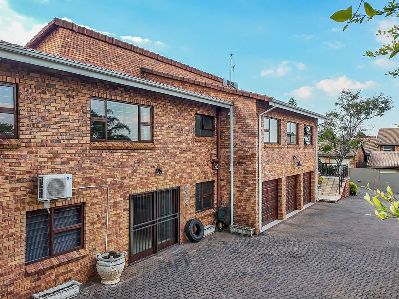 A well-maintained double-story face brick house featuring a spacious paved driveway and a triple garage, showcasing durable exterior finishes and clean architectural lines.
