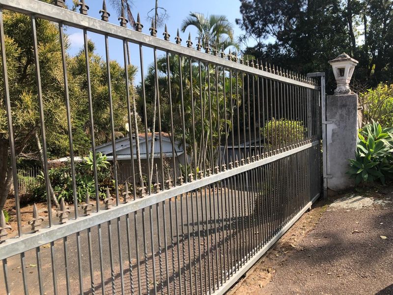 A view of the property entrance featuring a metal security gate mounted on a concrete pillar with an integrated light fixture.