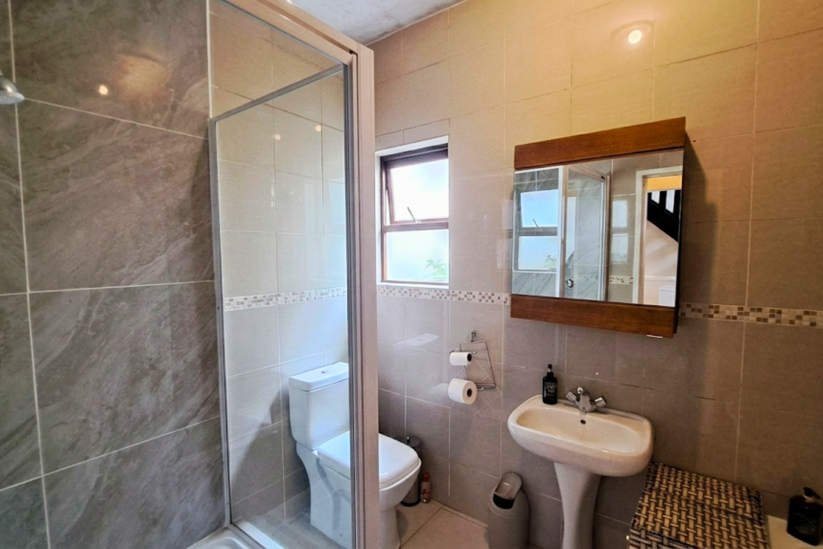 A functional bathroom featuring a glass-enclosed shower, pedestal basin, wall-mounted mirror cabinet, and tiled walls.