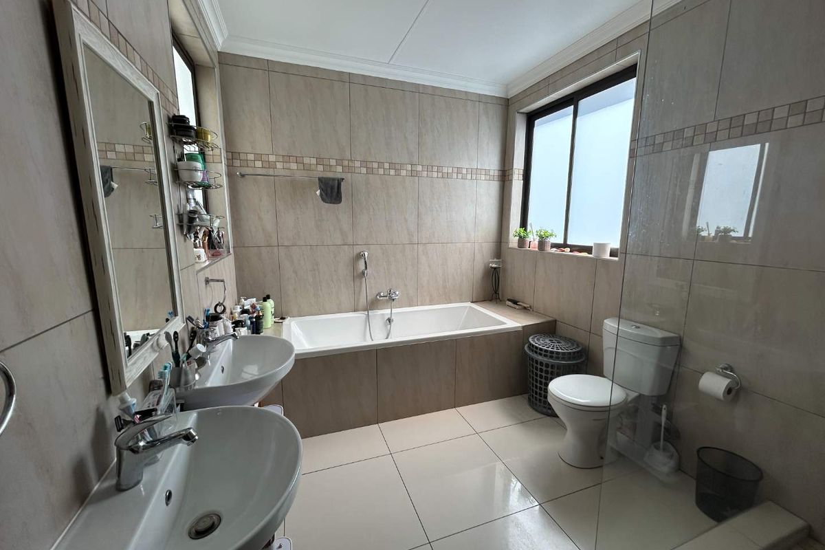 A well-appointed bathroom featuring a double vanity, built-in bathtub, and a separate shower area with a glass screen and neutral floor-to-ceiling tiling.