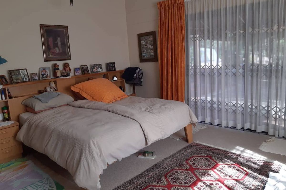A spacious bedroom featuring neutral wall tones, carpeted flooring, and large sliding glass doors with security gates providing access to the exterior.