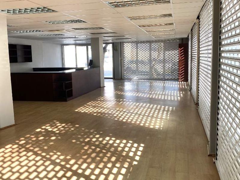 Spacious open-plan retail area featuring laminate flooring, suspended ceilings with recessed lighting, and secure roller shutters on the windows.