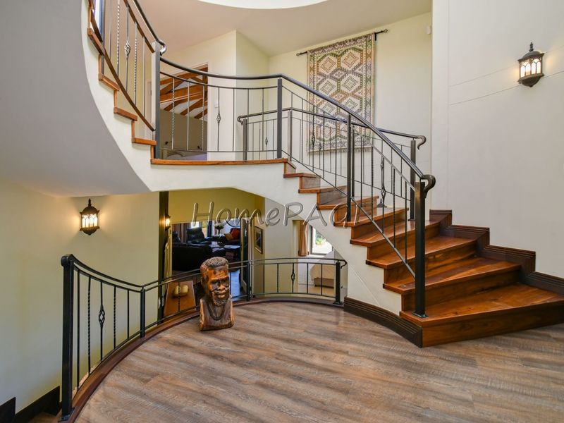 Grand entrance foyer featuring a striking curved timber staircase with decorative wrought iron balustrades and warm wall-mounted lighting.