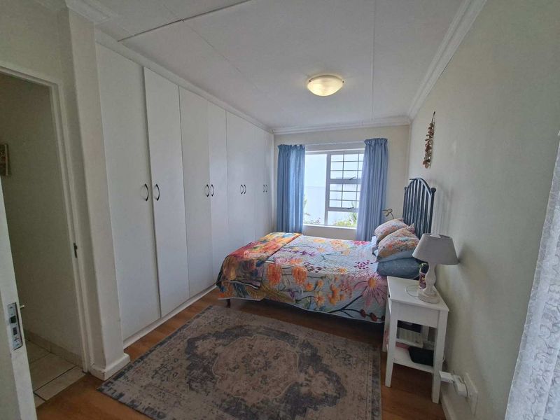 A functional bedroom featuring extensive built-in cupboards, laminated flooring, and a window providing natural light.