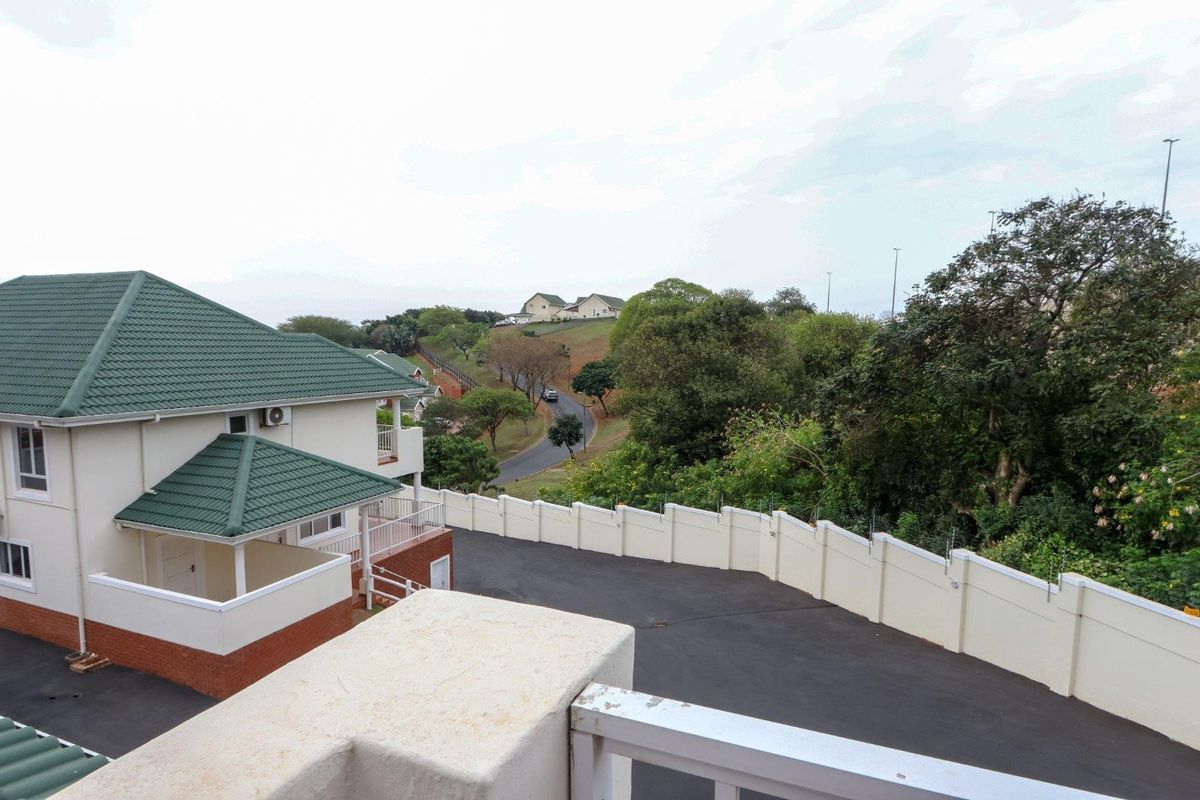 Elevated view of the townhouse complex featuring a green tiled roof, asphalt driveway, and secure perimeter wall with electric fencing.