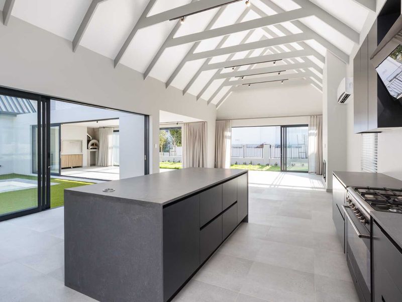 Spacious open-plan kitchen and living area featuring a vaulted ceiling with exposed rafters, modern island, and large sliding doors opening to the garden.