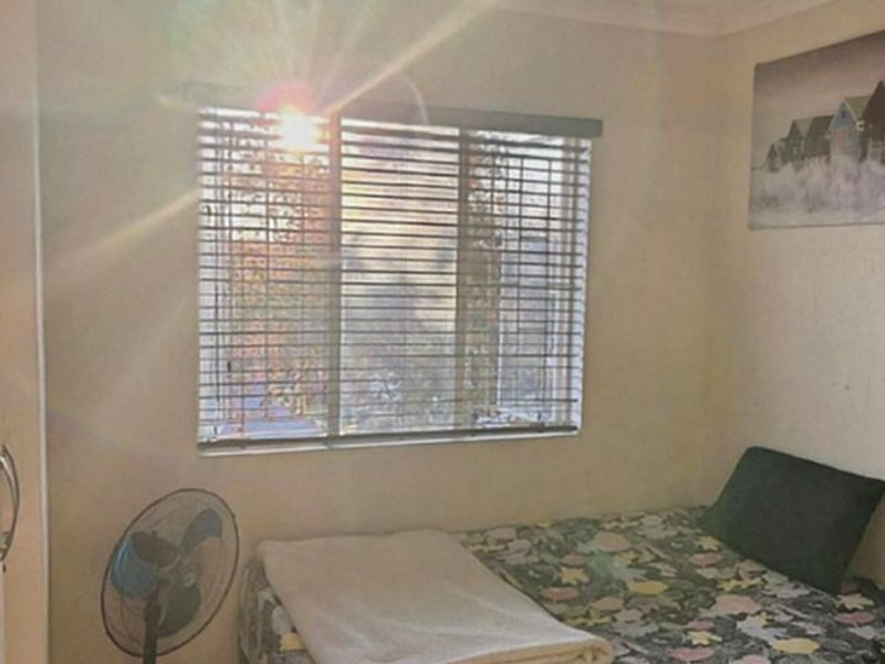 A compact bedroom featuring tiled flooring, a window with venetian blinds, and a central ceiling light fixture.