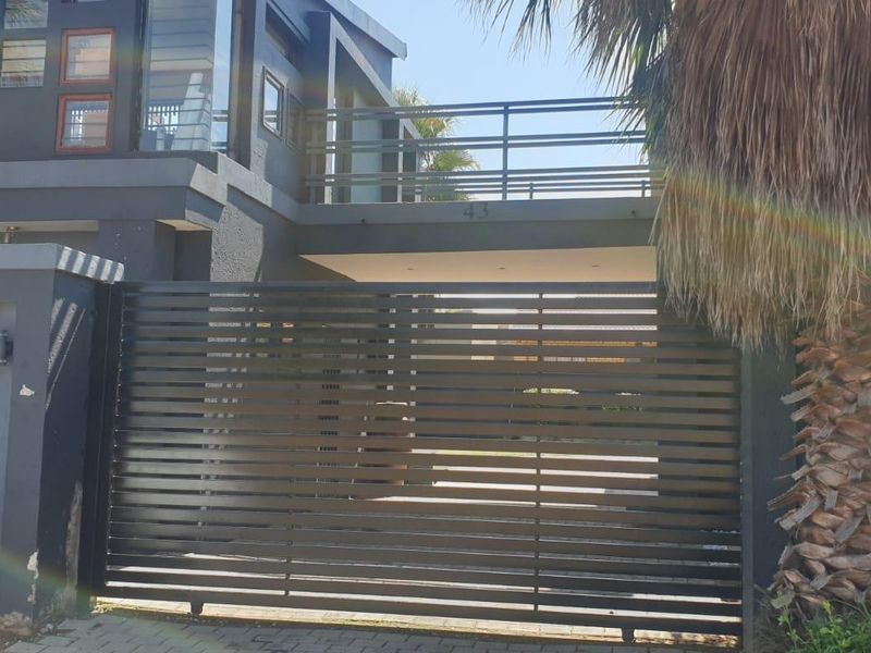 Front elevation of a modern two-story house featuring a dark exterior finish, a secure sliding gate, and an upper-level balcony.