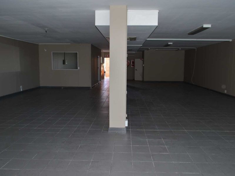 A spacious, empty open-plan commercial or utility area featuring tiled flooring, a central structural column, and basic fluorescent lighting.