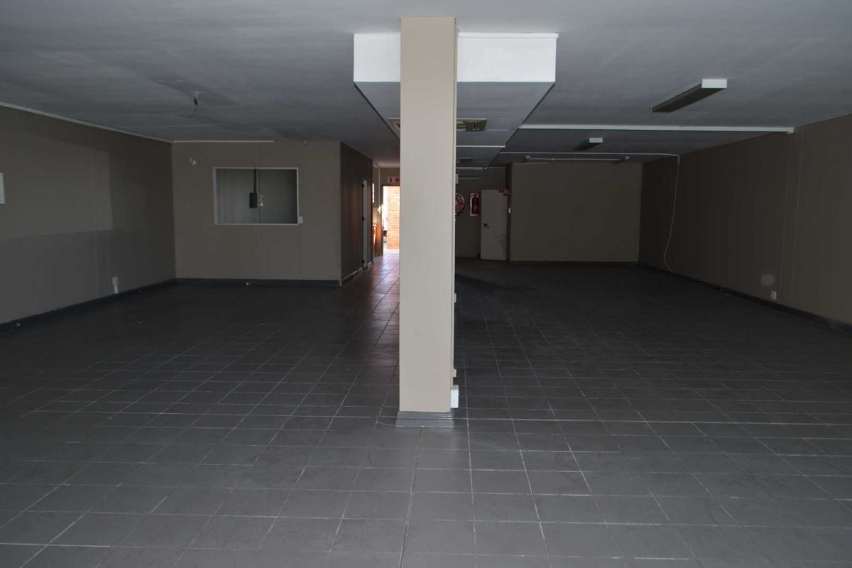 A spacious, empty open-plan commercial or utility area featuring tiled flooring, a central structural column, and basic fluorescent lighting.