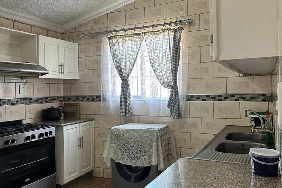 Functional kitchen featuring granite countertops, built-in cabinetry, gas stove with extractor fan, and tiled backsplash with neutral flooring.