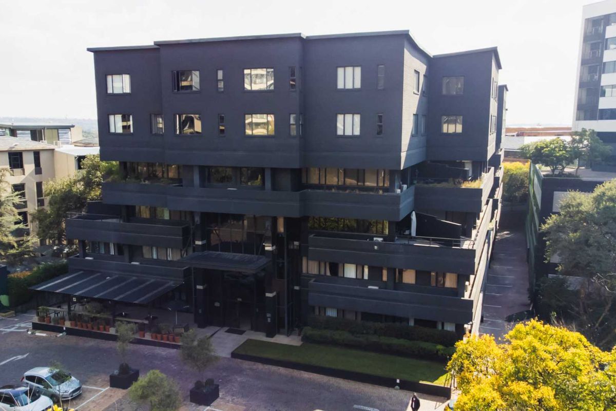 Aerial view of a modern multi-story apartment building featuring a dark facade, balconies, and ground-level parking area.