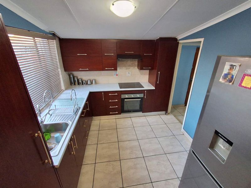 A functional kitchen featuring dark wood cabinetry, laminate countertops, integrated oven and hob, and tiled flooring.