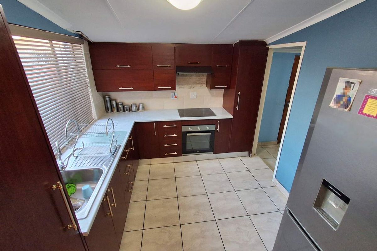 A functional kitchen featuring dark wood cabinetry, laminate countertops, integrated oven and hob, and tiled flooring.