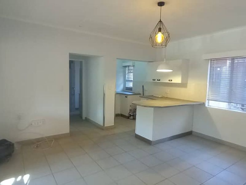 An open-plan living and kitchen area featuring tiled flooring, a breakfast bar island, and neutral finishes, offering a blank canvas for personalization.