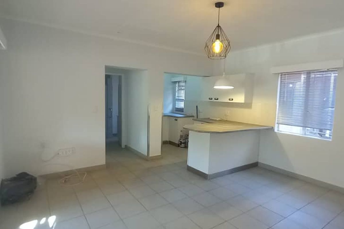 An open-plan living and kitchen area featuring tiled flooring, a breakfast bar island, and neutral finishes, offering a blank canvas for personalization.