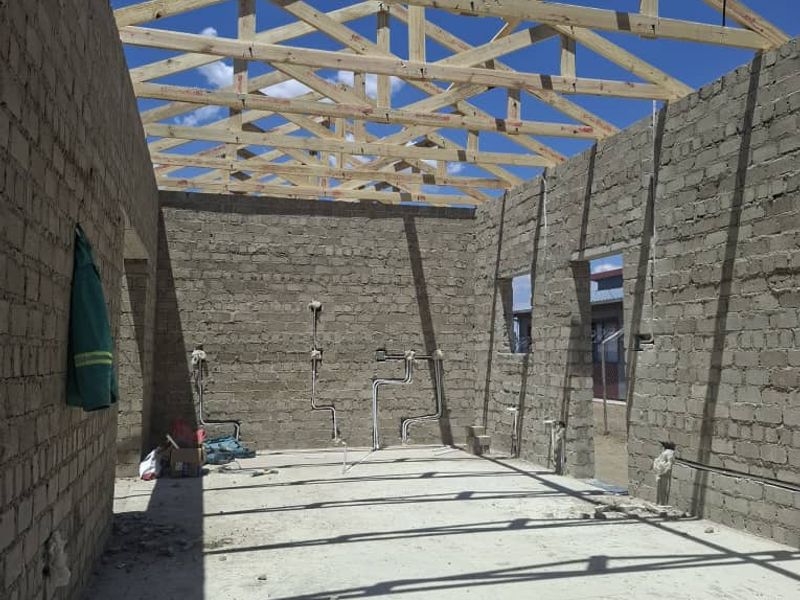 An unfinished construction site showing exposed timber roof trusses, concrete block walls, and exposed electrical and plumbing infrastructure.