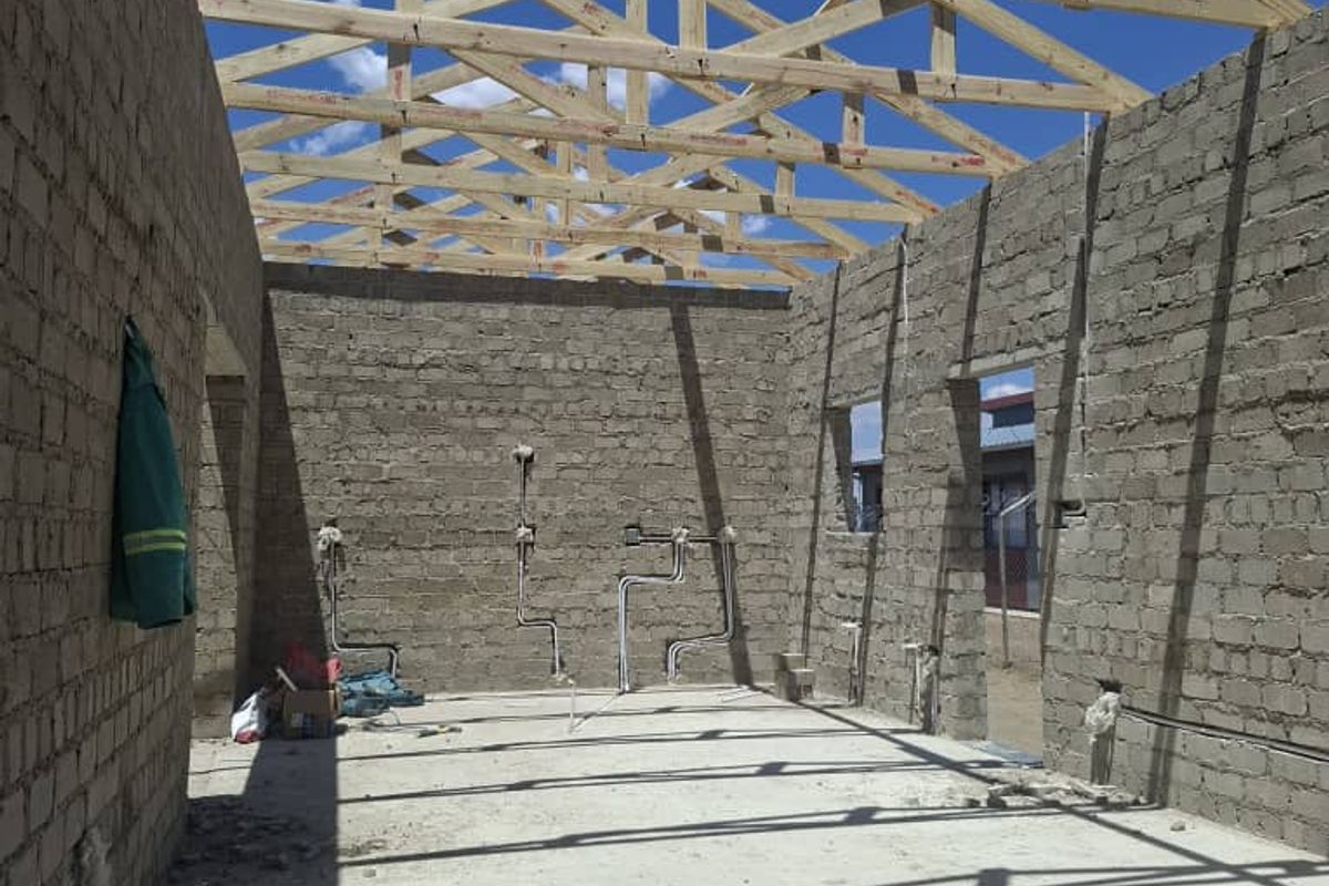 An unfinished construction site showing exposed timber roof trusses, concrete block walls, and exposed electrical and plumbing infrastructure.