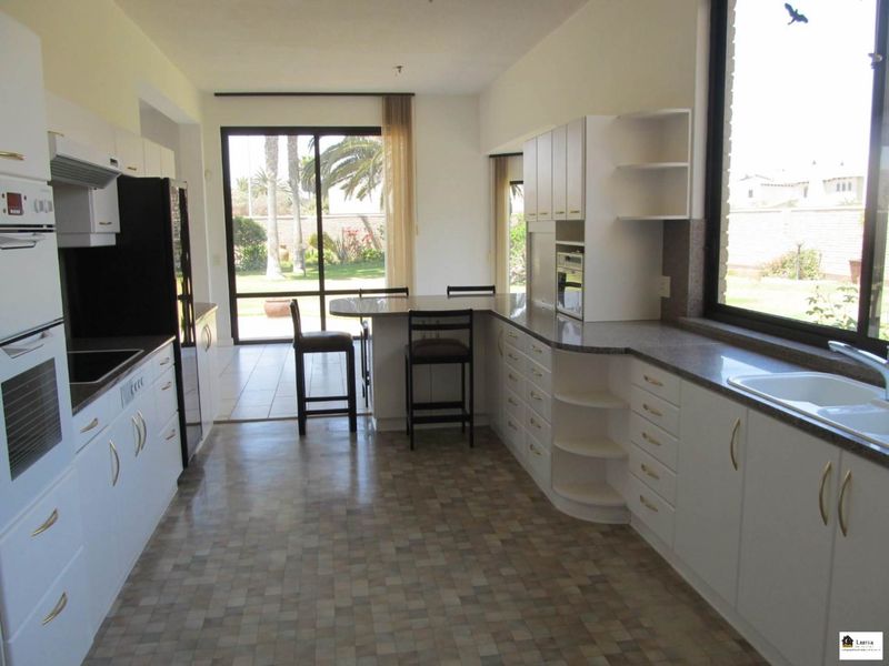 A functional kitchen featuring white cabinetry, granite countertops, and a breakfast bar, with direct access to the rear garden through sliding glass doors.