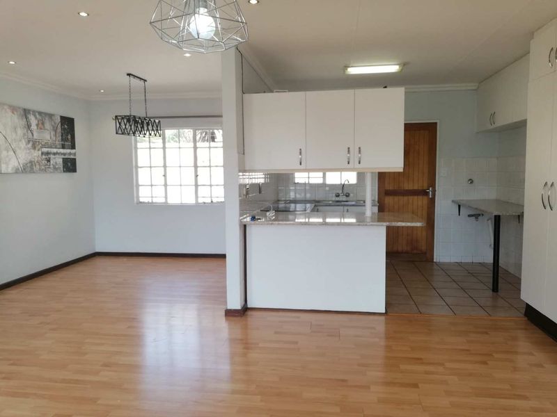 Open-plan living and kitchen area featuring laminate flooring, built-in white cabinetry, granite countertops, and recessed lighting in a neutral, vacant space.
