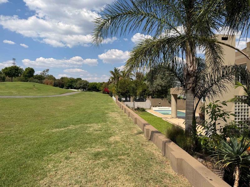 A view of the rear garden featuring a swimming pool, a retaining wall, and a well-maintained lawn adjacent to an open green space.