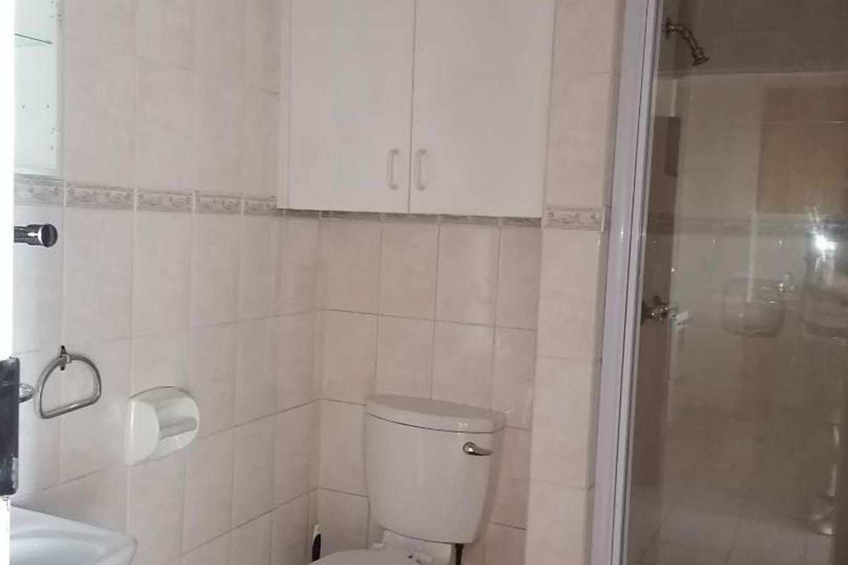 A functional bathroom featuring a shower enclosure, toilet, pedestal basin, and built-in wall storage cabinet with neutral tiled finishes.
