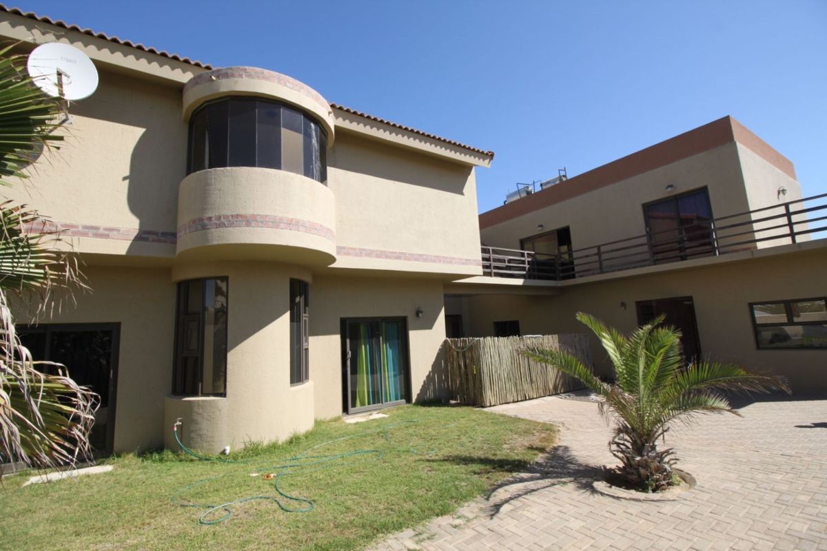 Rear view of a multi-story house featuring a curved architectural design, balcony, paved courtyard, and small garden area.