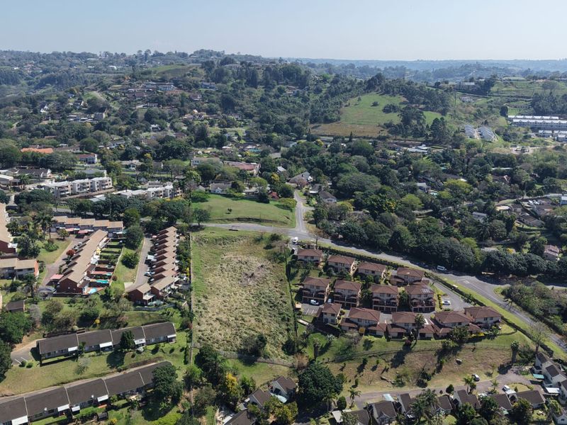 An aerial view of a vacant residential plot situated within an established suburban neighborhood, showcasing surrounding housing developments and local infrastructure.