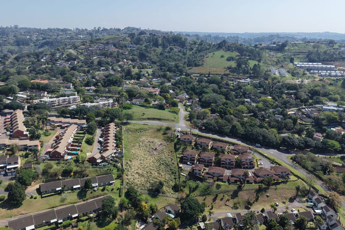 An aerial view of a vacant residential plot situated within an established suburban neighborhood, showcasing surrounding housing developments and local infrastructure.