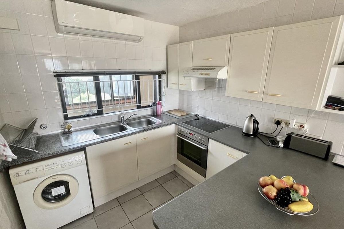 Functional kitchen featuring built-in cabinetry, integrated oven, electric hob, extractor fan, double sink, and wall-mounted air conditioning unit.