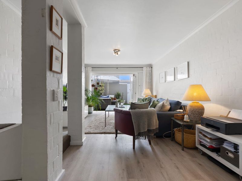 A bright living room featuring laminate flooring, painted brick walls, and sliding glass doors that open onto an outdoor patio area.