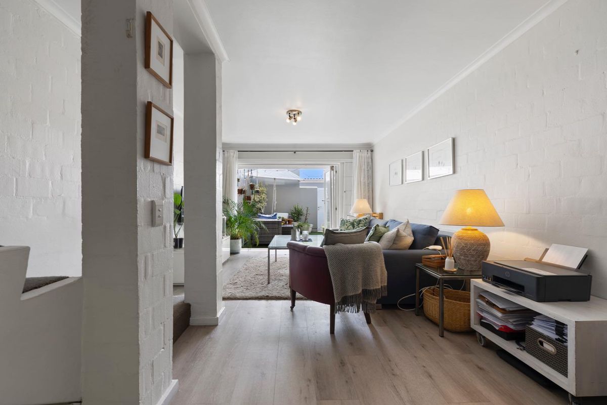 A bright living room featuring laminate flooring, painted brick walls, and sliding glass doors that open onto an outdoor patio area.