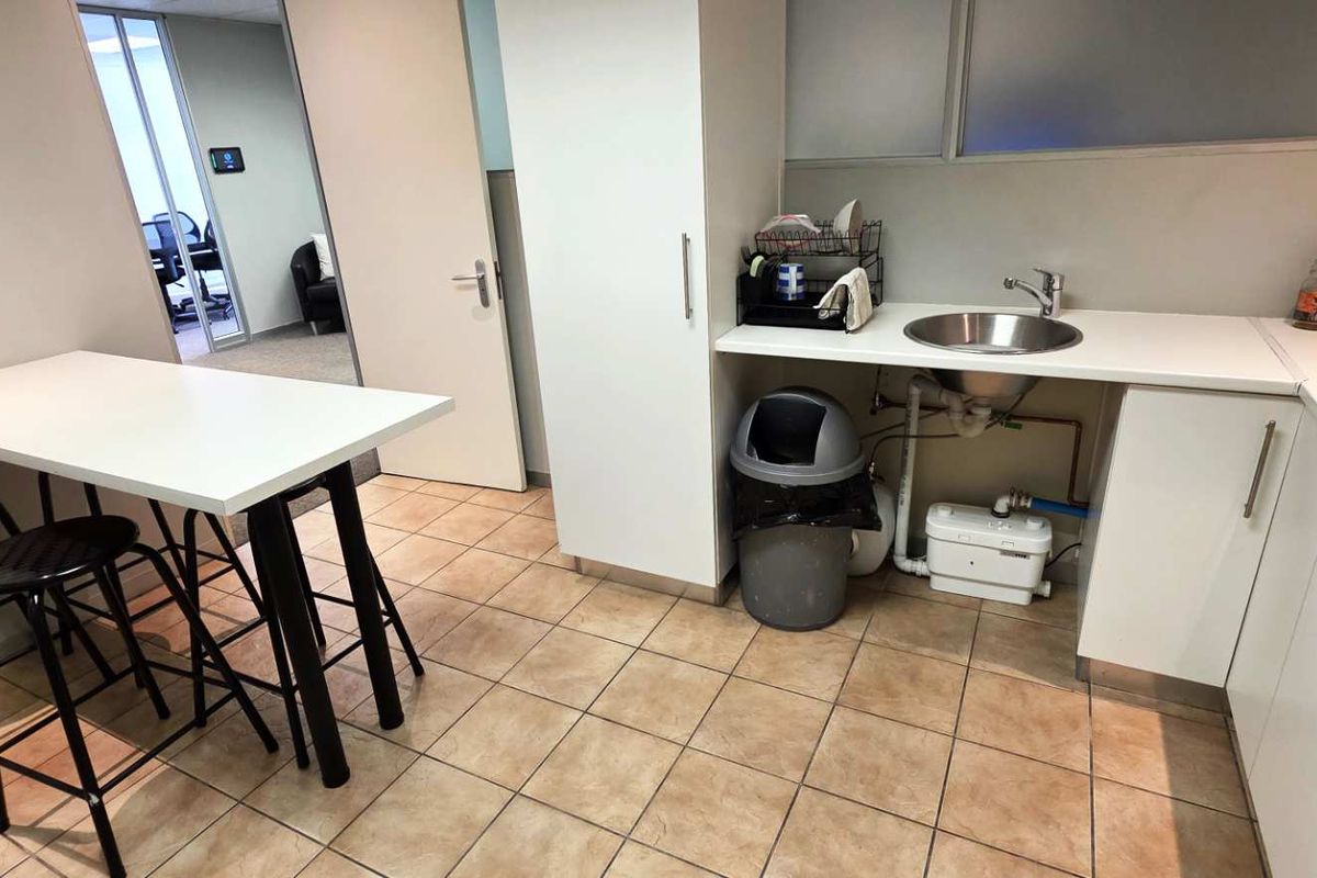 A compact office kitchenette featuring white cabinetry, a stainless steel sink, and tiled flooring, providing a functional break area within the workspace.
