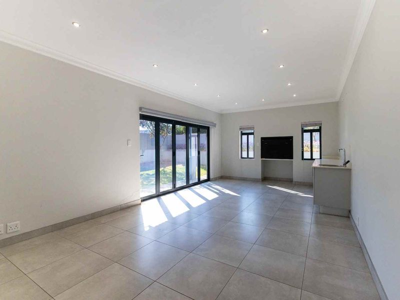 Spacious open-plan living area featuring large bi-fold doors, neutral tiled flooring, recessed lighting, and a convenient built-in sink unit.